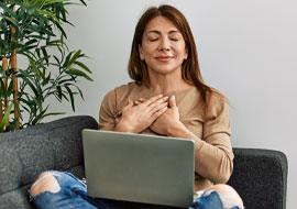 woman sitting on a couch with laptop on lap and hands on chest