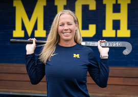 Field Hockey Coach holding a field hockey stick behind her head