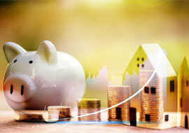 A piggy bank, stacks of coins and a wooden house toy